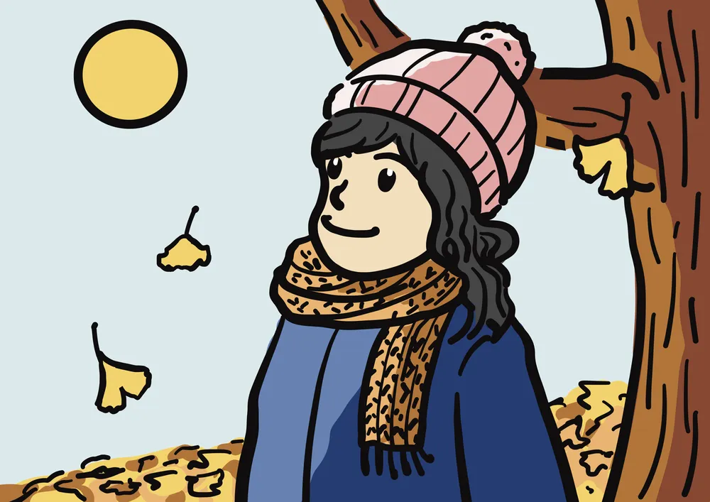 イチョウの木の下にニット帽を被って、マフラーをしている女性。太陽の光で照らされている様子。暖かい光。